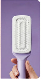 Hairbrush with collected hair on one side and a hand holding a purple hairbrush on the other, against a white background.